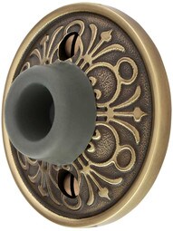 Wall-Mount Door Stop with Lancaster Rosette and Rubber Bumper in Antique Brass.